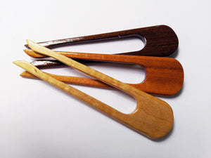 three wooden hair sticks laying next to each other ranging in color from dark to light wood