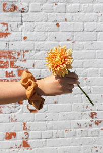 someone holding a large flower with a silk scrunchie on their wrist