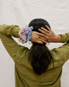 a woman putting a gauze scrunchie in her hair, she has multiple scrunchies on her wrist of varying colors