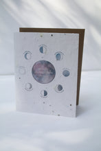 Load image into Gallery viewer, a plantable seed card - the card has a textured look from the seeds imbedded in the paper. There is a drawing of the moon phases on the card in an indigo color. The moon phases are surrounding one large moon in the center that reads "wishing you many more moons"