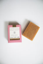 Load image into Gallery viewer, a bar of holiday soap by Little Seed Farm next to the box it comes in. The box has red and white stripes on it.