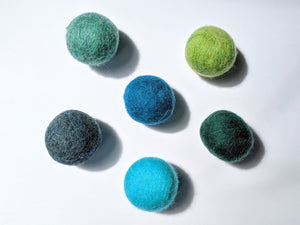 5 wool dryer balls that are cool toned varying from light blue an green, to dark blue and green