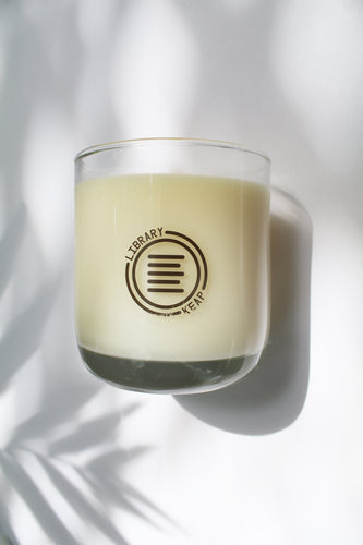 an up close video of a candle - the candle wax is a white color and is inside a clear glass container that doubles as a drinking tumbler once the candle burns out.