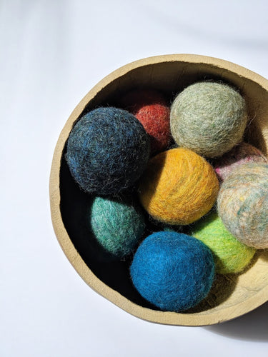 a wooden bowl full of wool dryer balls in all different colors. the wool dryer balls are about the size of a baseball.