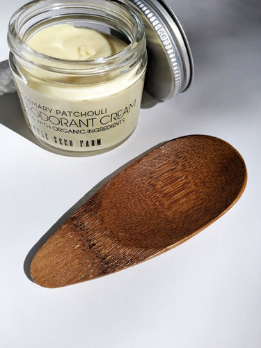 a wooden bamboo applicator next to a jar of deodorant. The applicator looks smooth and curved. 