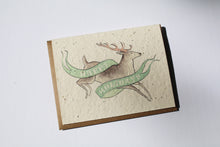 Load image into Gallery viewer, a plantable seed card - the card has a textured look from the seeds imbedded in the paper. There is a deer drawing on this one that says &quot;HAPPY HOLIDAYS&quot; on a green banner going across the deer
