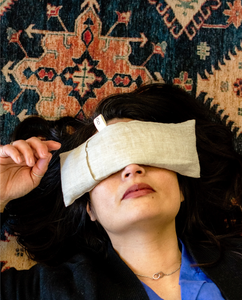 a woman laying down with a natural linen eye pillow resting on her eyes