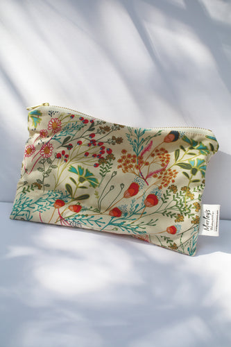 a cream colored cosmetic bag with a gold zipper and summery floral pattern