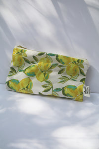 a cream colored cosmetic bag with a gold zipper and lemon design