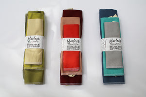 three different color reusable wrapping paper bundles (from left to right: green, red, and blue)